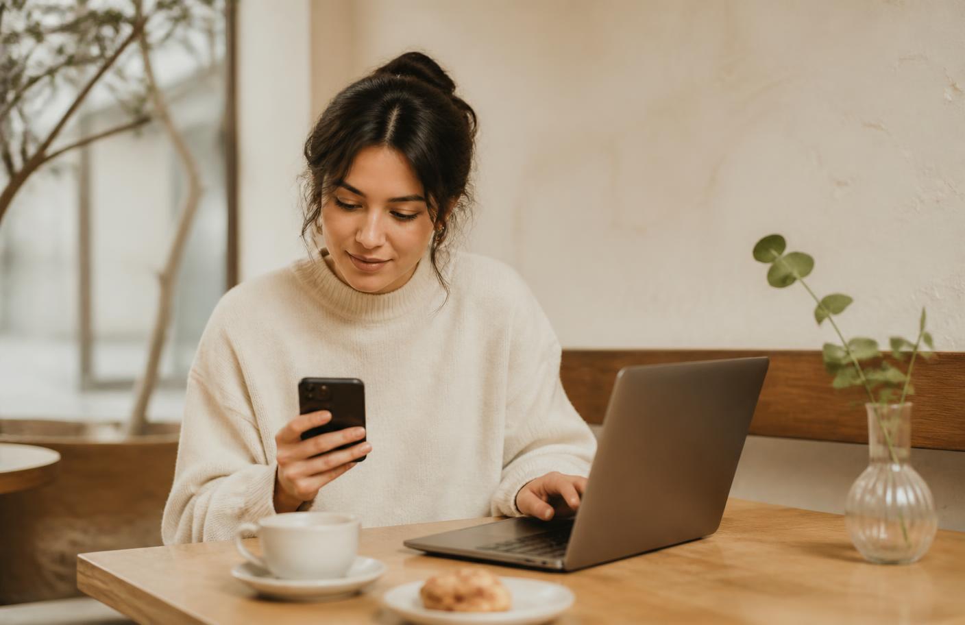Sole trader using a phone and laptop side by side at a café table