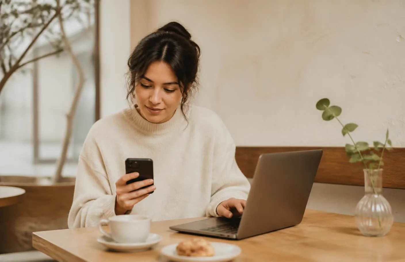 Sole trader using a phone and laptop side by side at a café table