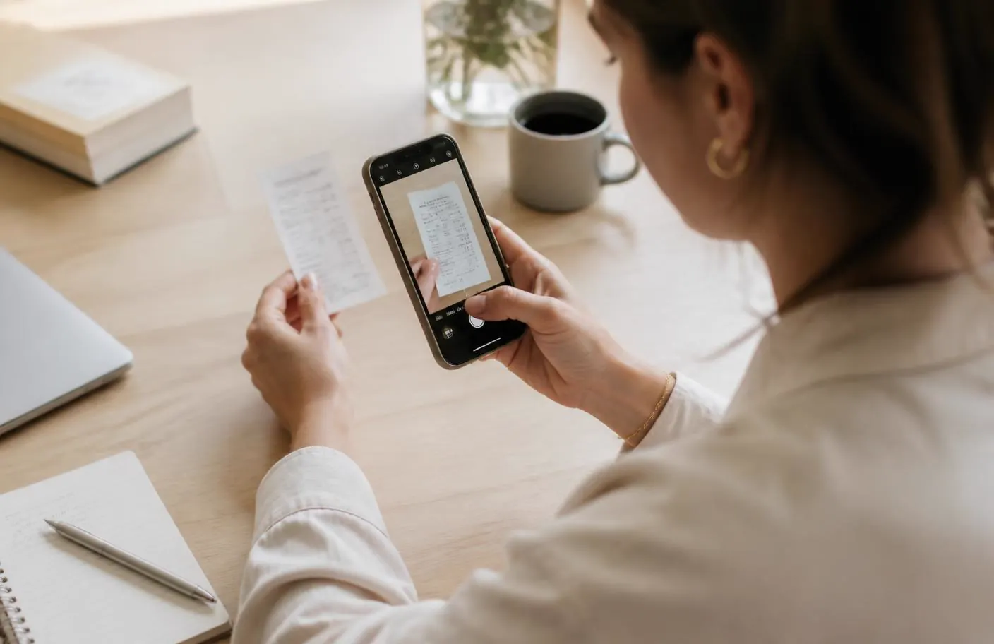 Sole trader photographing a paper receipt with a smartphone at a light wooden desk