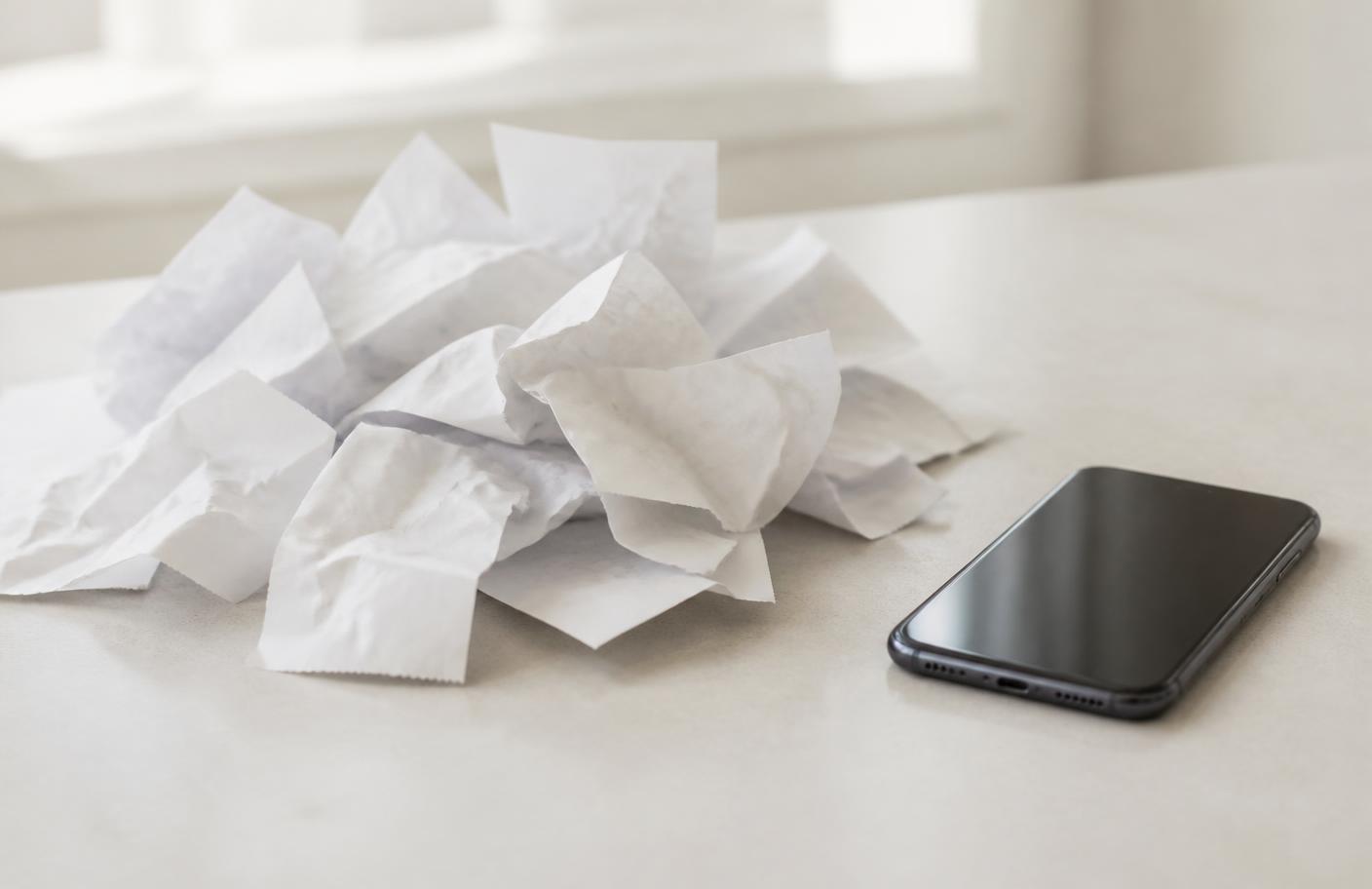 A pile of paper receipts beside a smartphone on a light table